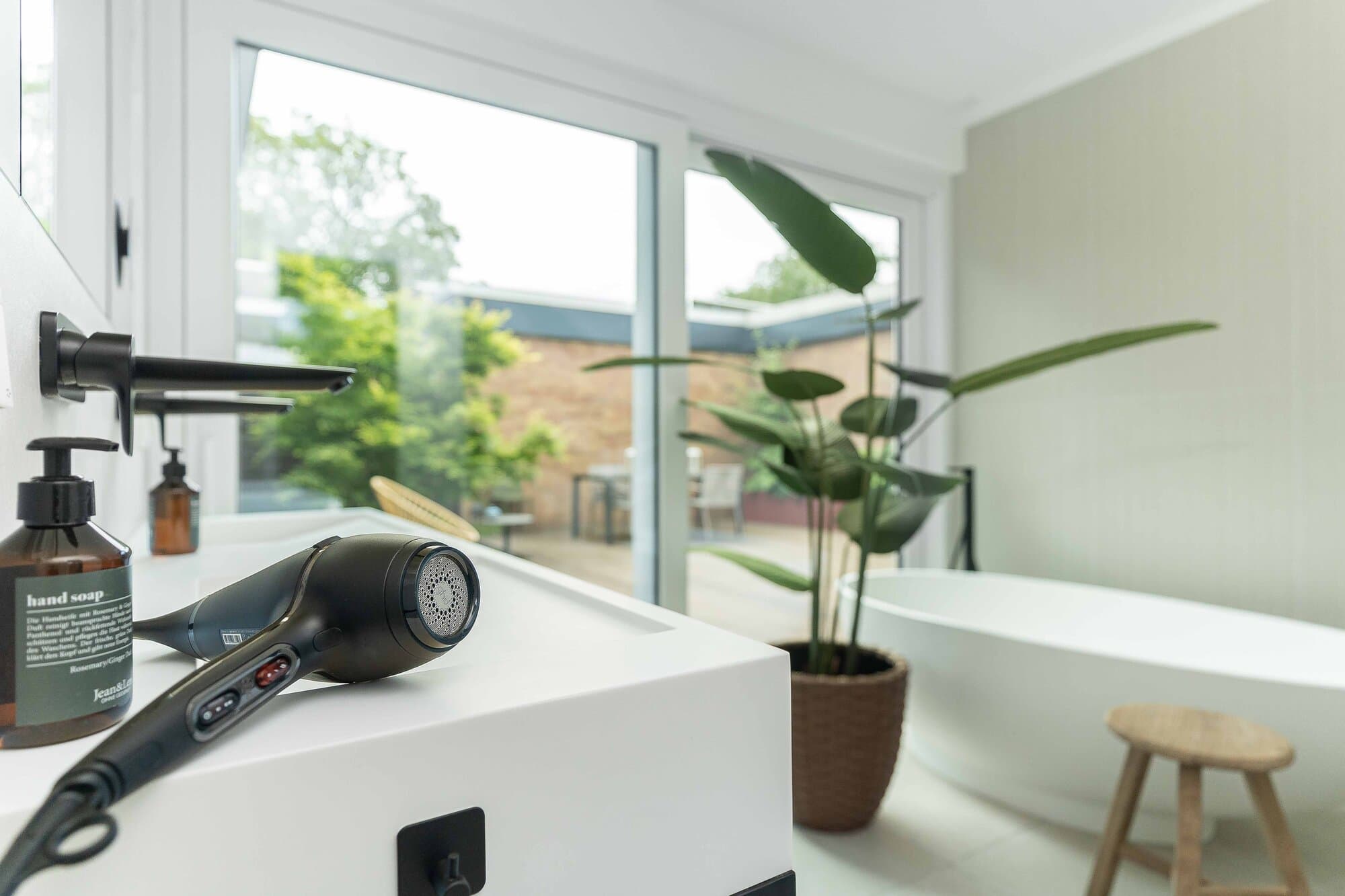 Detail im Masterbad, Föhn und Handseife auf dem Waschtisch, Strelitzie vor der bodentiefen Fensterfront zum Innenhof