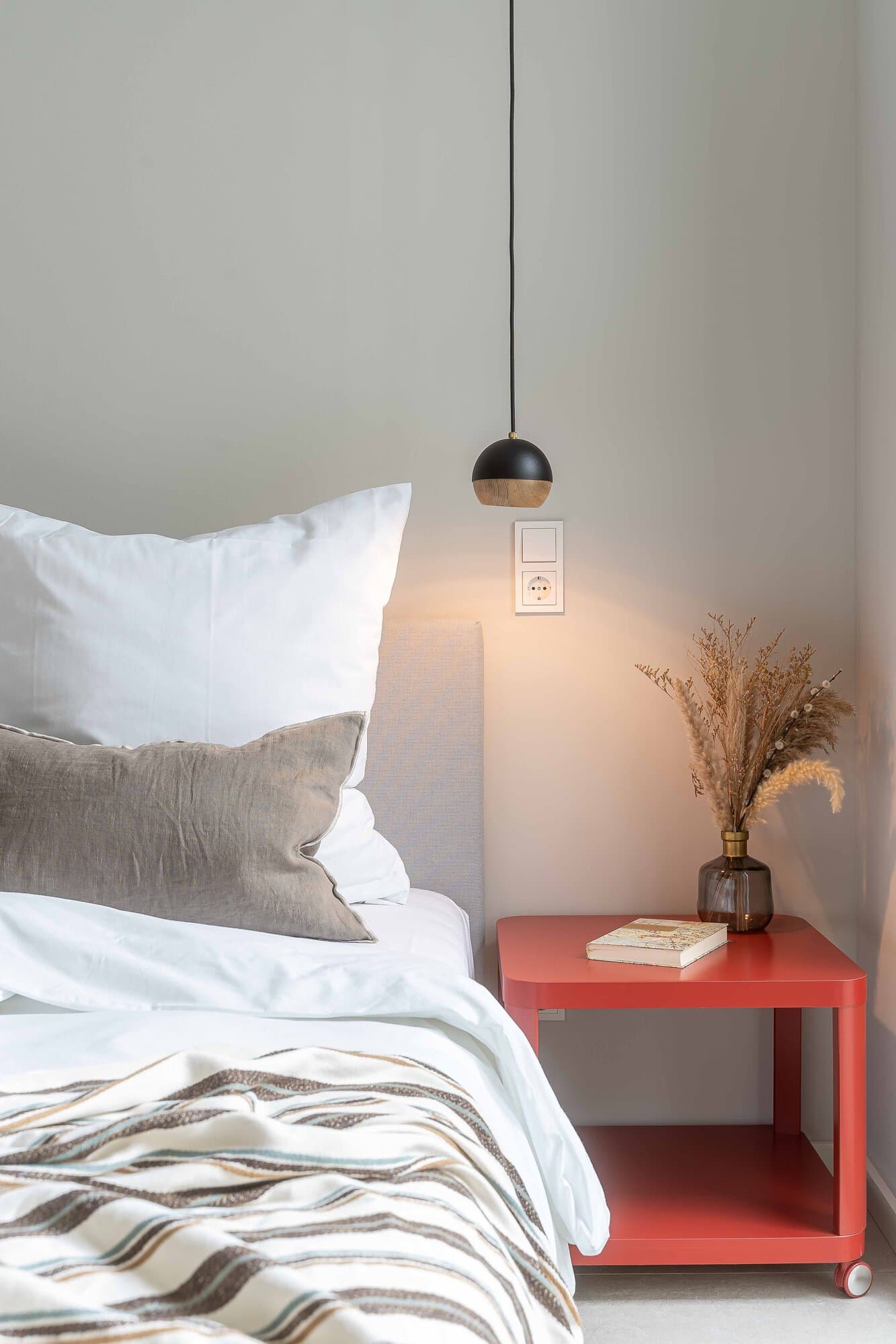 Detailansicht des Master-Schlafzimmers mit rotem Rollcontainer als Nachttisch und Pampasgras in Glasvase