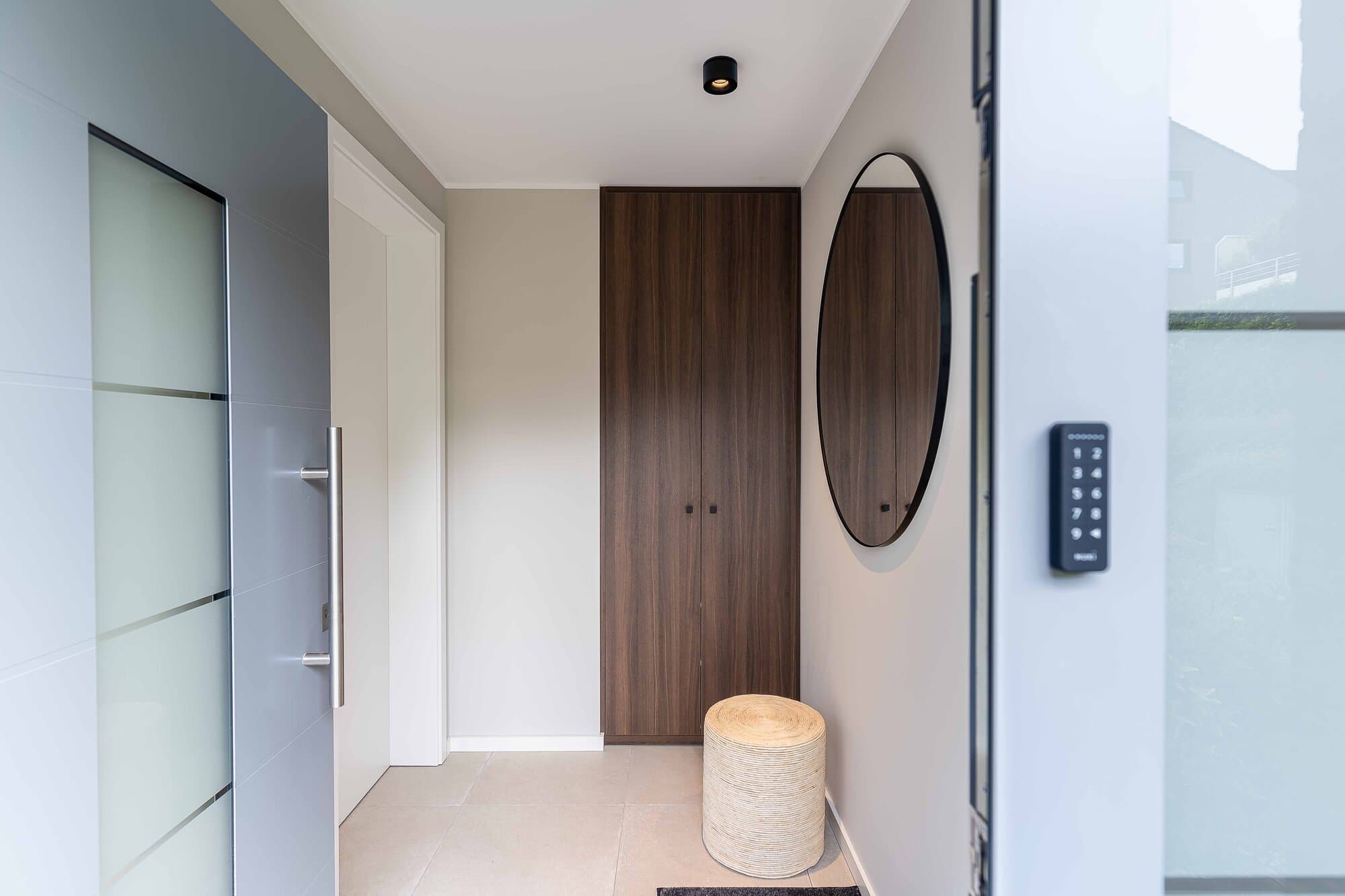 Schlüsselloser Self-Check-in im Bungalow Ratingen, Eingangsbereich mit Walnuss-Einbauschrank, rundem Spiegel und Keypad an der Eingangstür