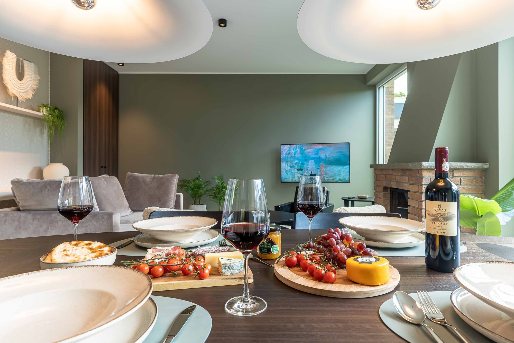 Gedeckter Esstisch mit Wein, Käse und Brot, Blick durch den offenen Wohnbereich