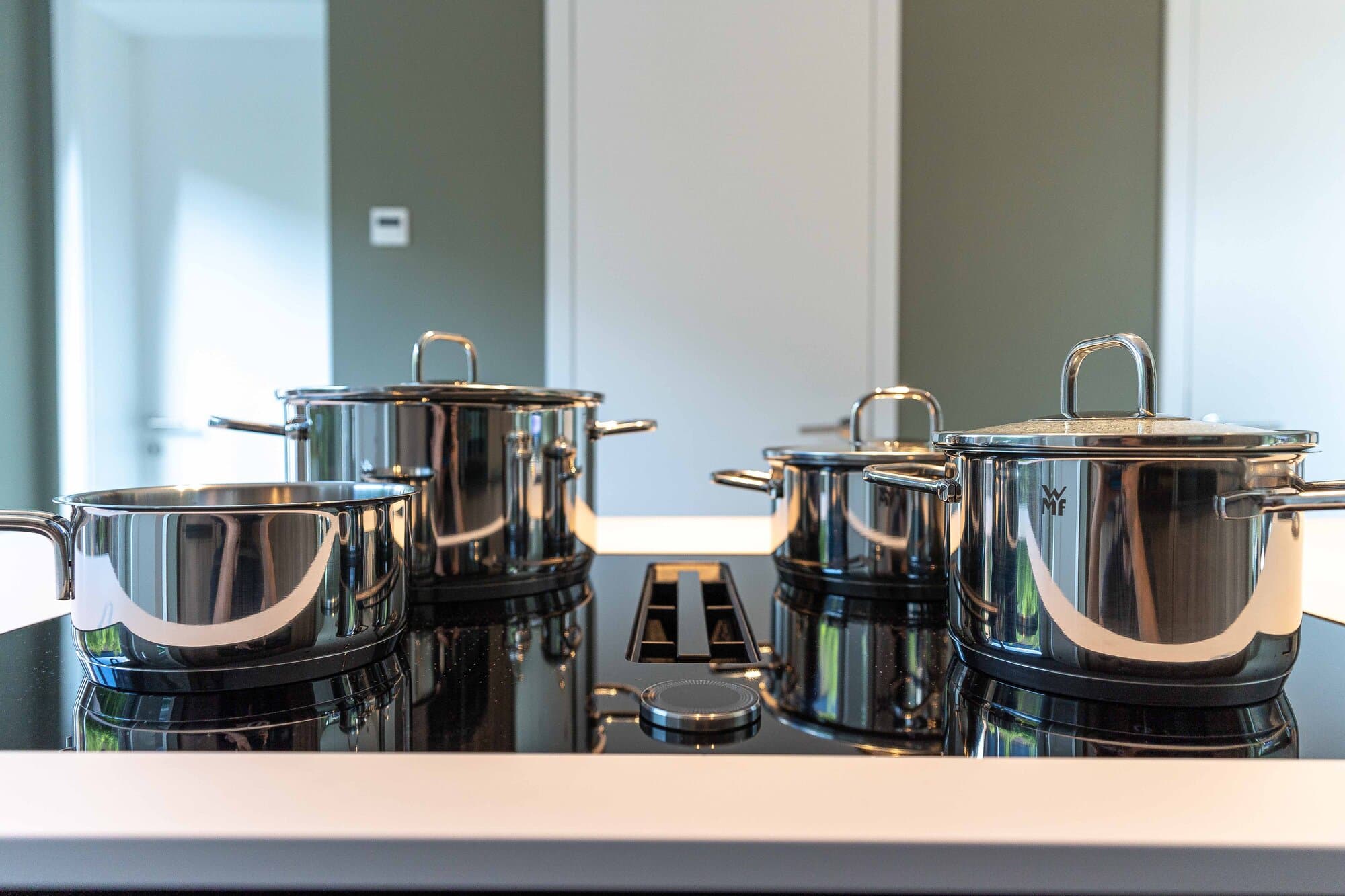 Vier WMF-Edelstahltöpfe auf dem Induktionskochfeld der Kücheninsel, voll ausgestattet für mehrgängige Menüs