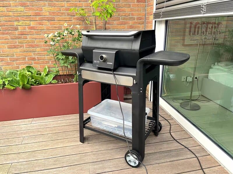 Elektrogrill auf Holzdeck-Terrasse vor Klinkerwand mit Kletterpflanzen, BBQ-Ecke im Innenhof des Bungalow Ratingen
